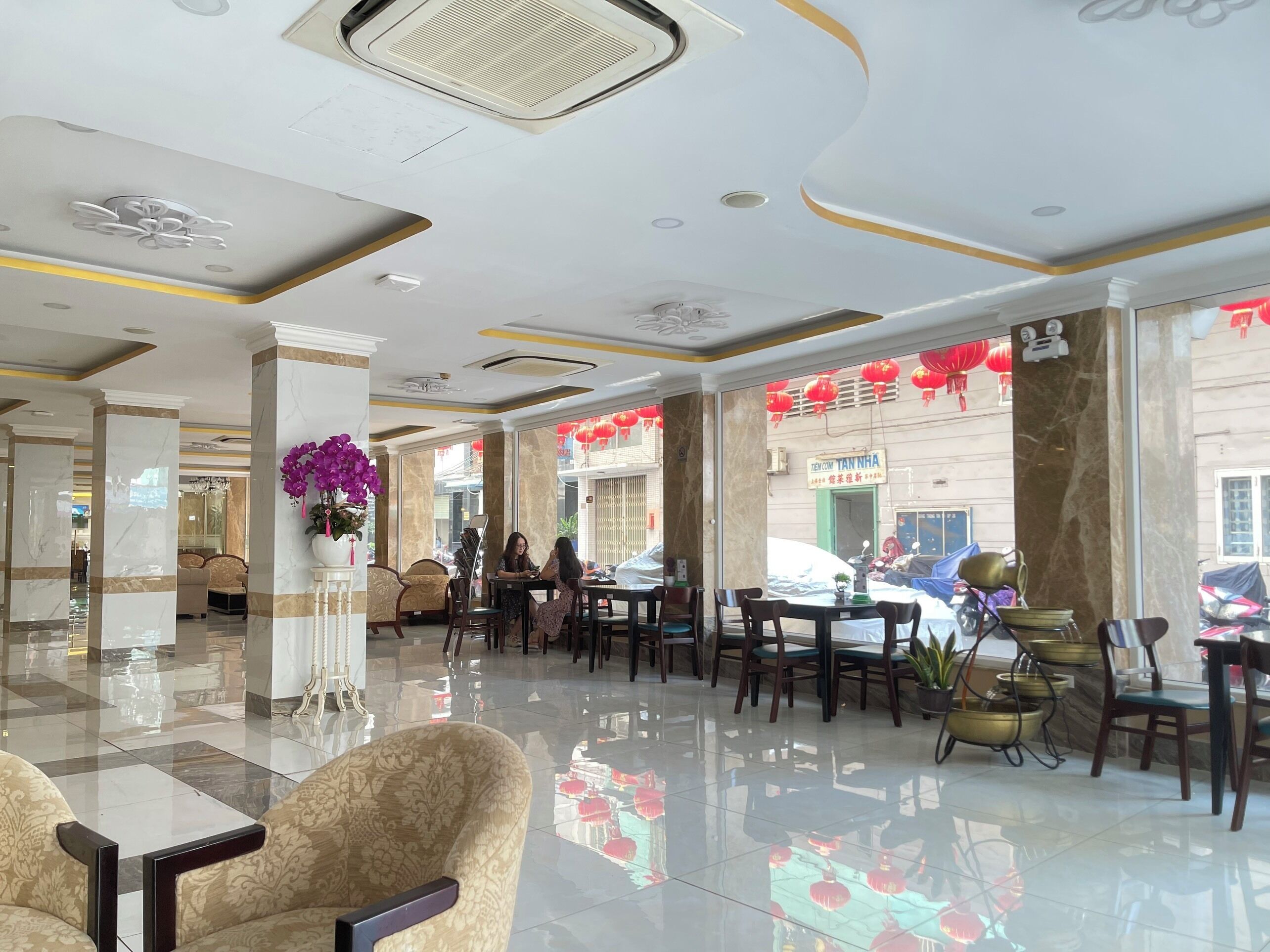 A spacious lobby with marble columns, a central floral arrangement, and a view of the street outside.