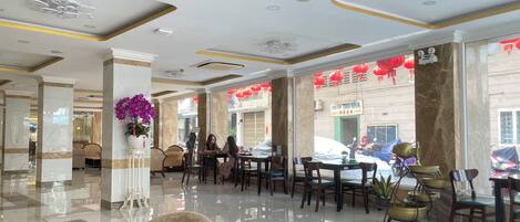 A spacious lobby with marble columns, a central floral arrangement, and a view of the street outside.