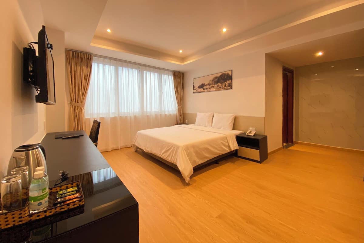 Ein Hotelzimmer mit Bett, Nachttisch, Schreibtisch, Stuhl und einem an der Wand befestigten Fernseher.