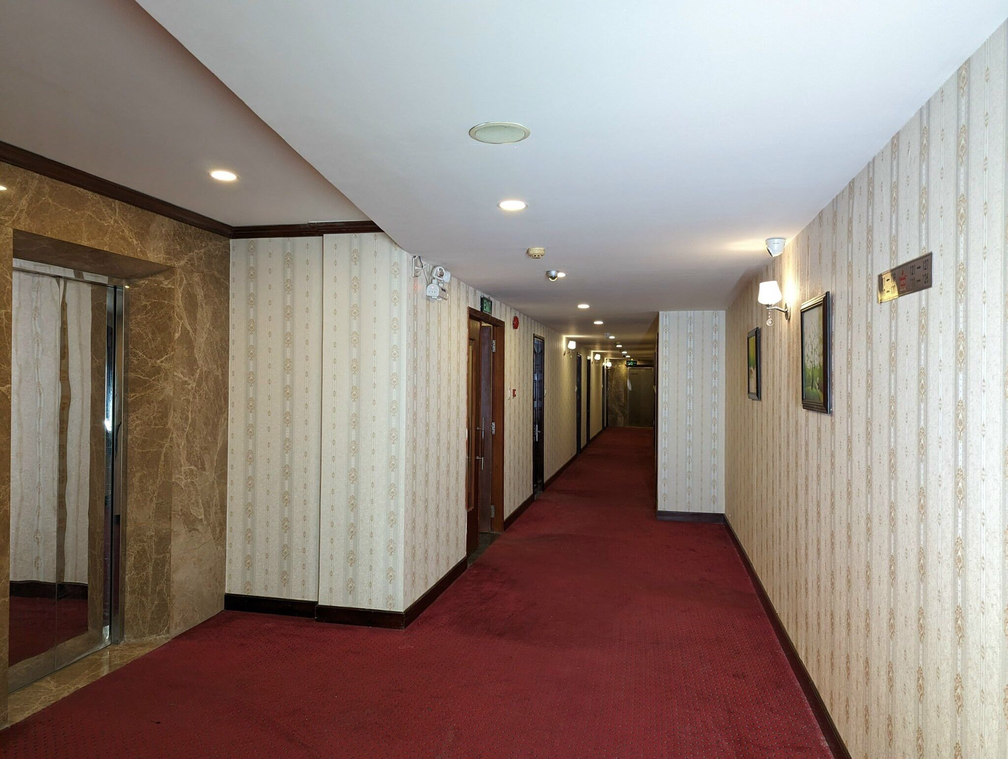 Un pasillo de hotel con papel tapiz estampado, alfombra roja y varias puertas.