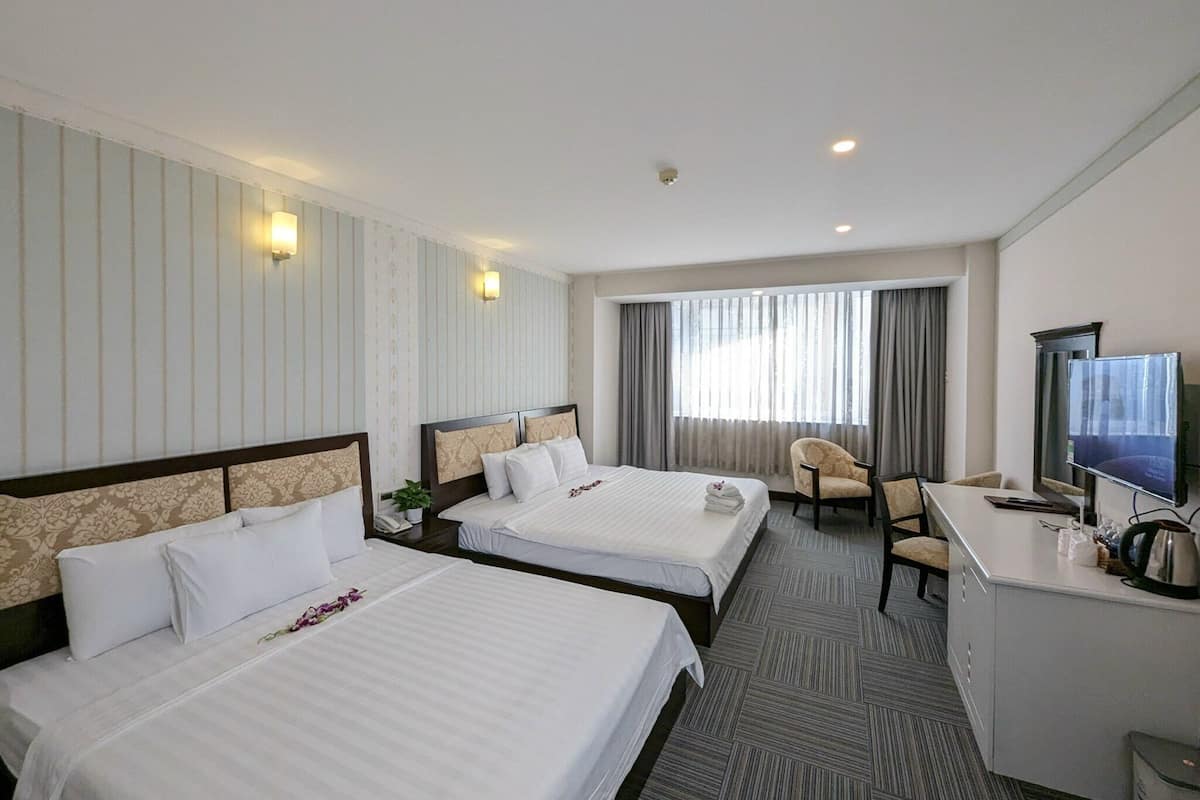 Ein Hotelzimmer mit zwei Betten, einem Schreibtisch, einem Stuhl, einem Fernseher und einem Vorhangfenster.