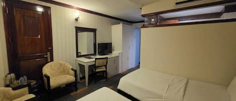 A hotel room with two beds, a desk with a television, a chair, a wardrobe, and an air conditioning unit.