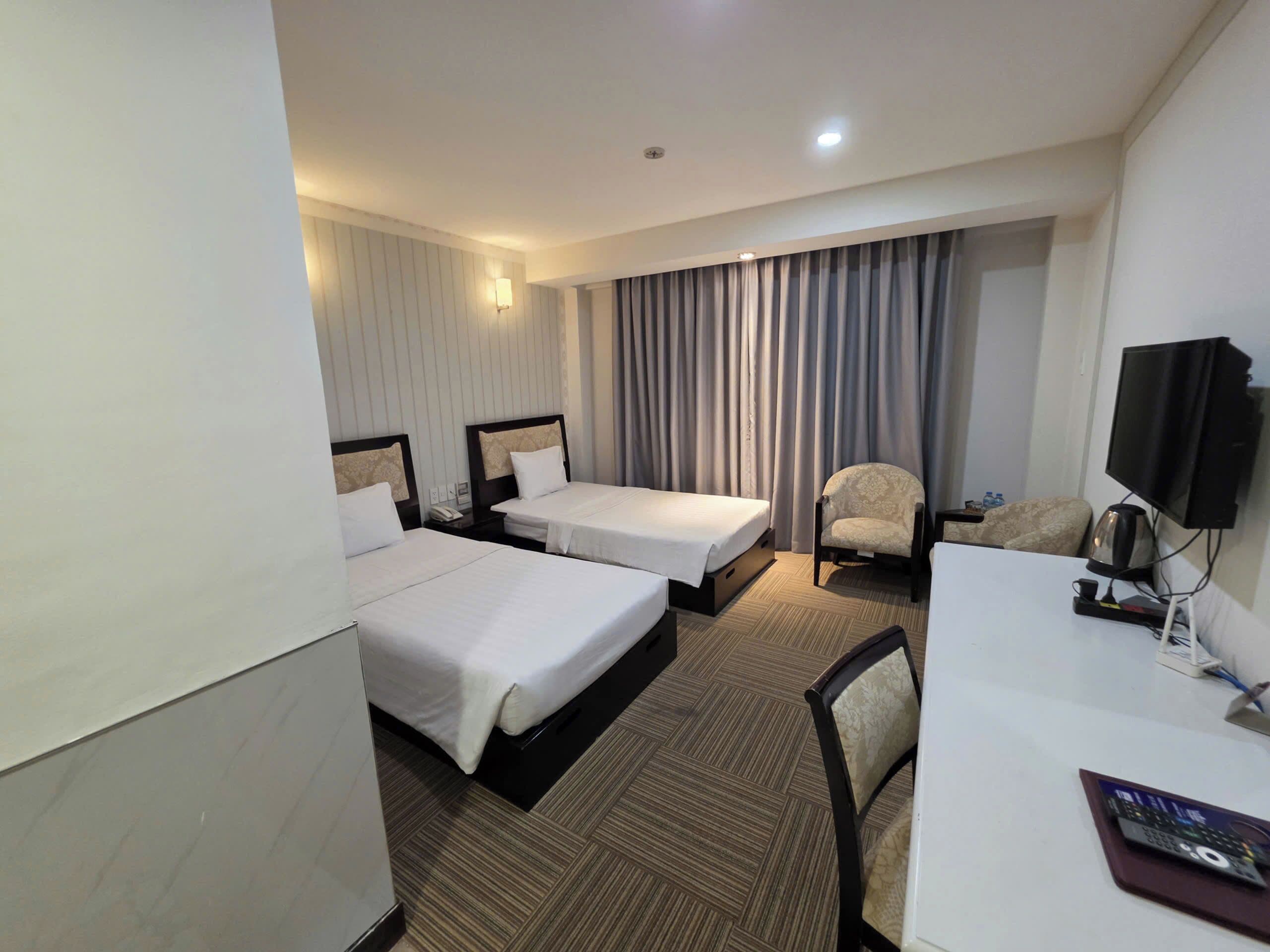 A hotel room with two beds, a desk, a chair, a television, and a window with curtains.