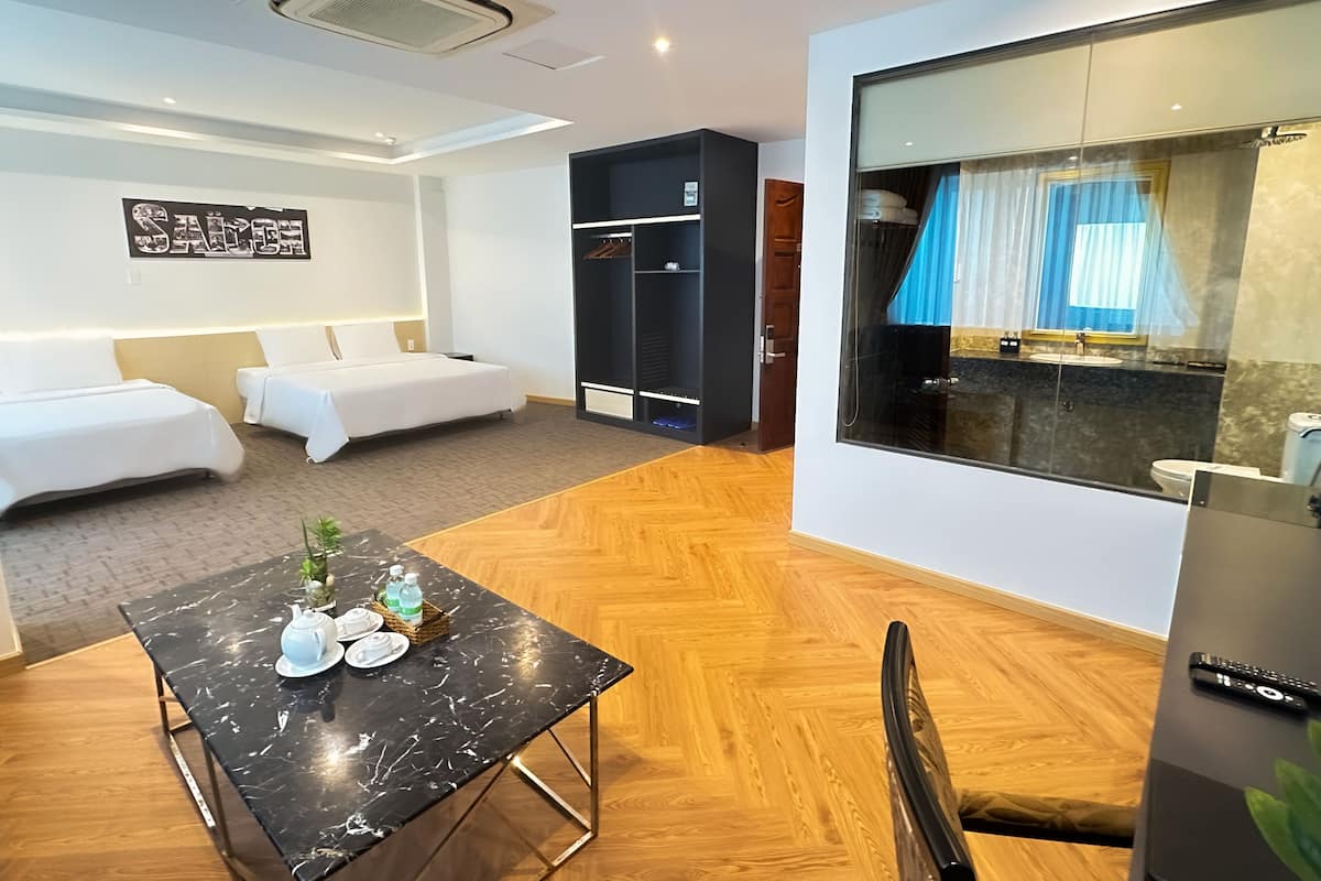 Ein Hotelzimmer mit einem Bett, einem kleinen Tisch mit Teekanne und Tassen, einem Kleiderschrank und einem Badezimmer mit Spiegel und Vorhängen.