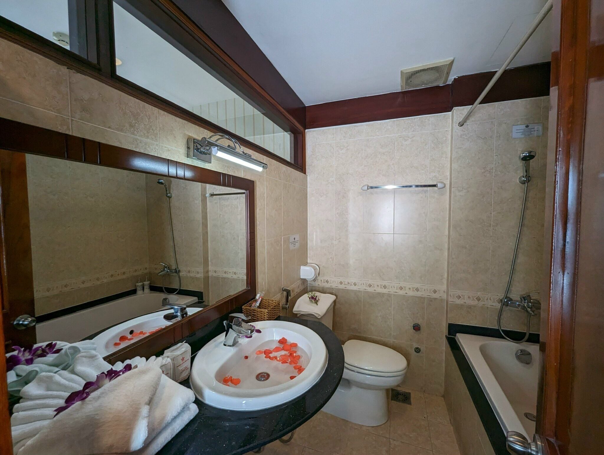 Une salle de bain avec un grand miroir, une baignoire, des toilettes et un lavabo décoré de pétales de rose.
