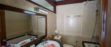 Une salle de bain avec un grand miroir, une baignoire, des toilettes et un lavabo décoré de pétales de rose.