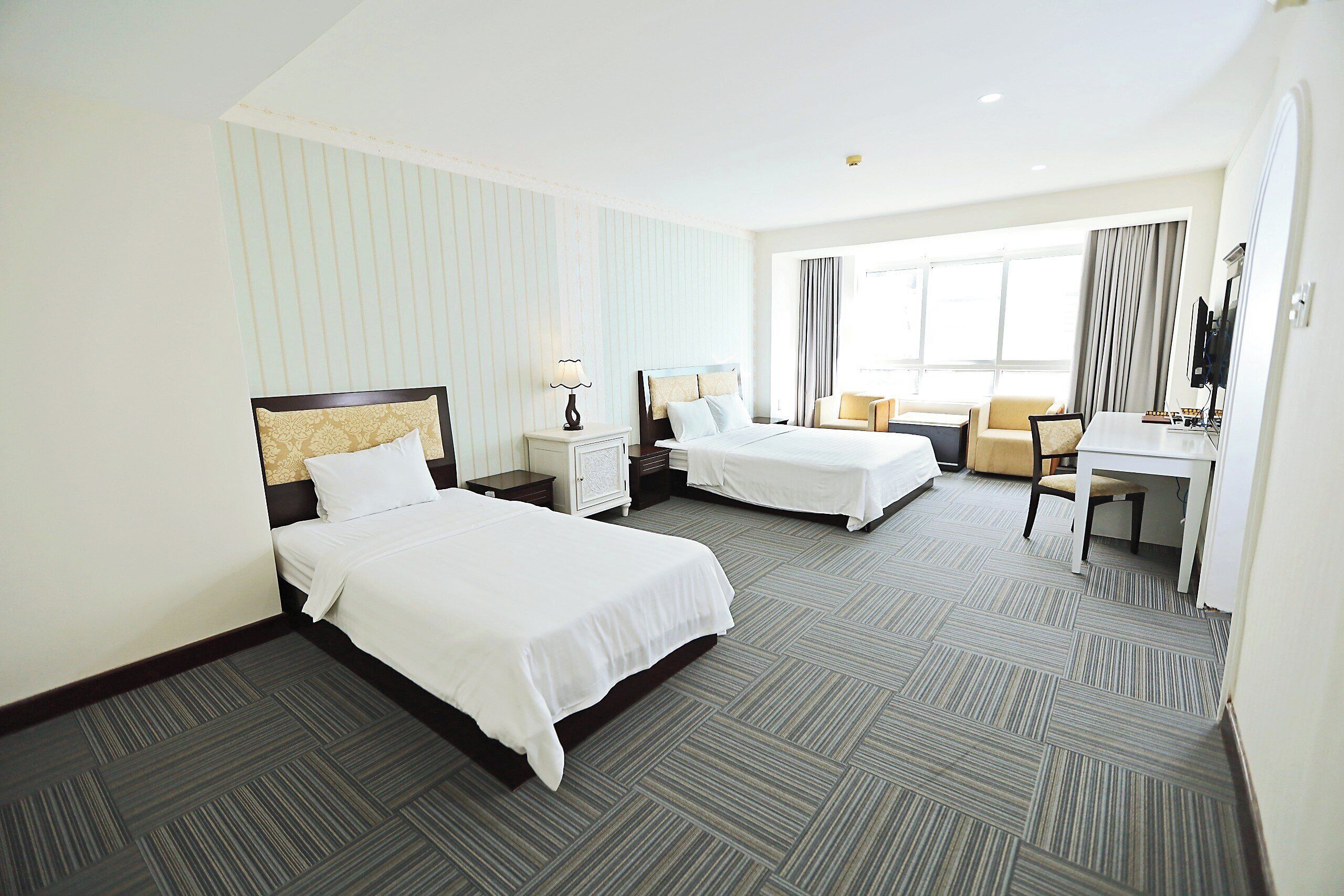 A hotel room with two beds, a desk, a chair, and a TV.