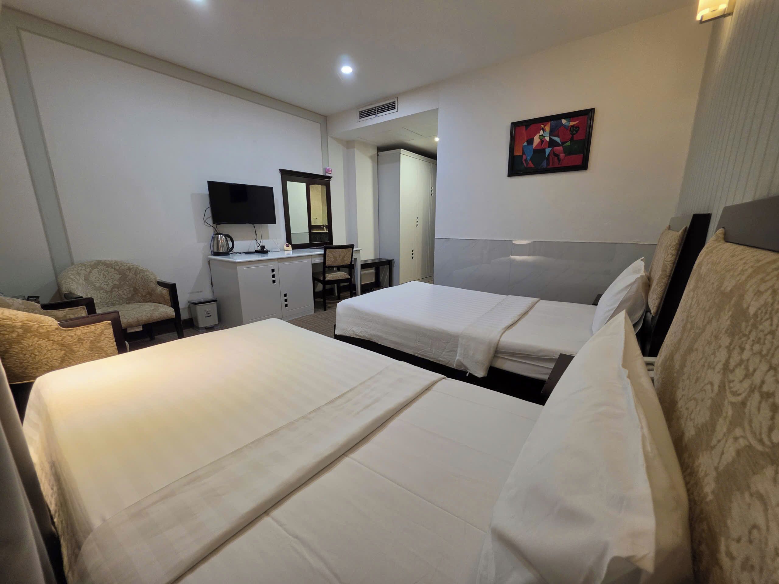Habitación de hotel con dos camas, un escritorio con una silla, televisión y un cuadro en la pared.