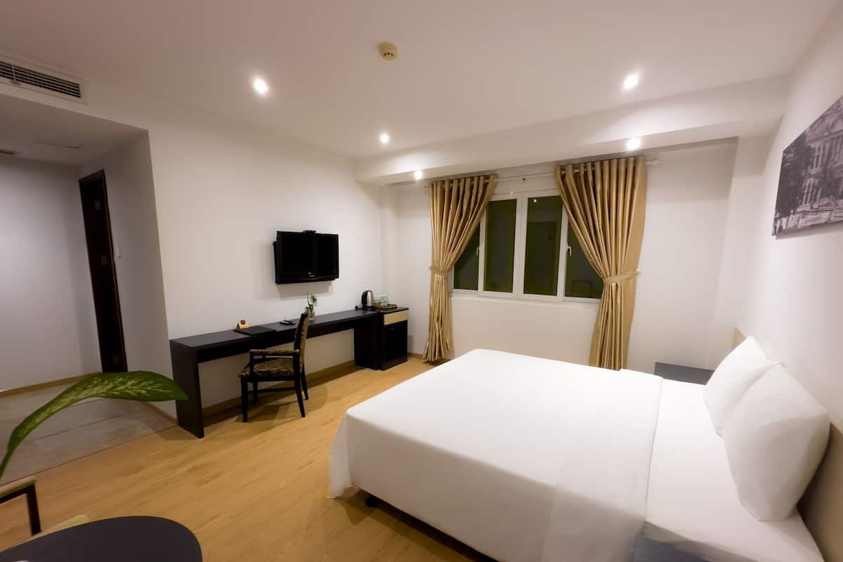 Ein Hotelzimmer mit Bett, Schreibtisch, Stuhl, Fernseher und einem Fenster mit Vorhängen.