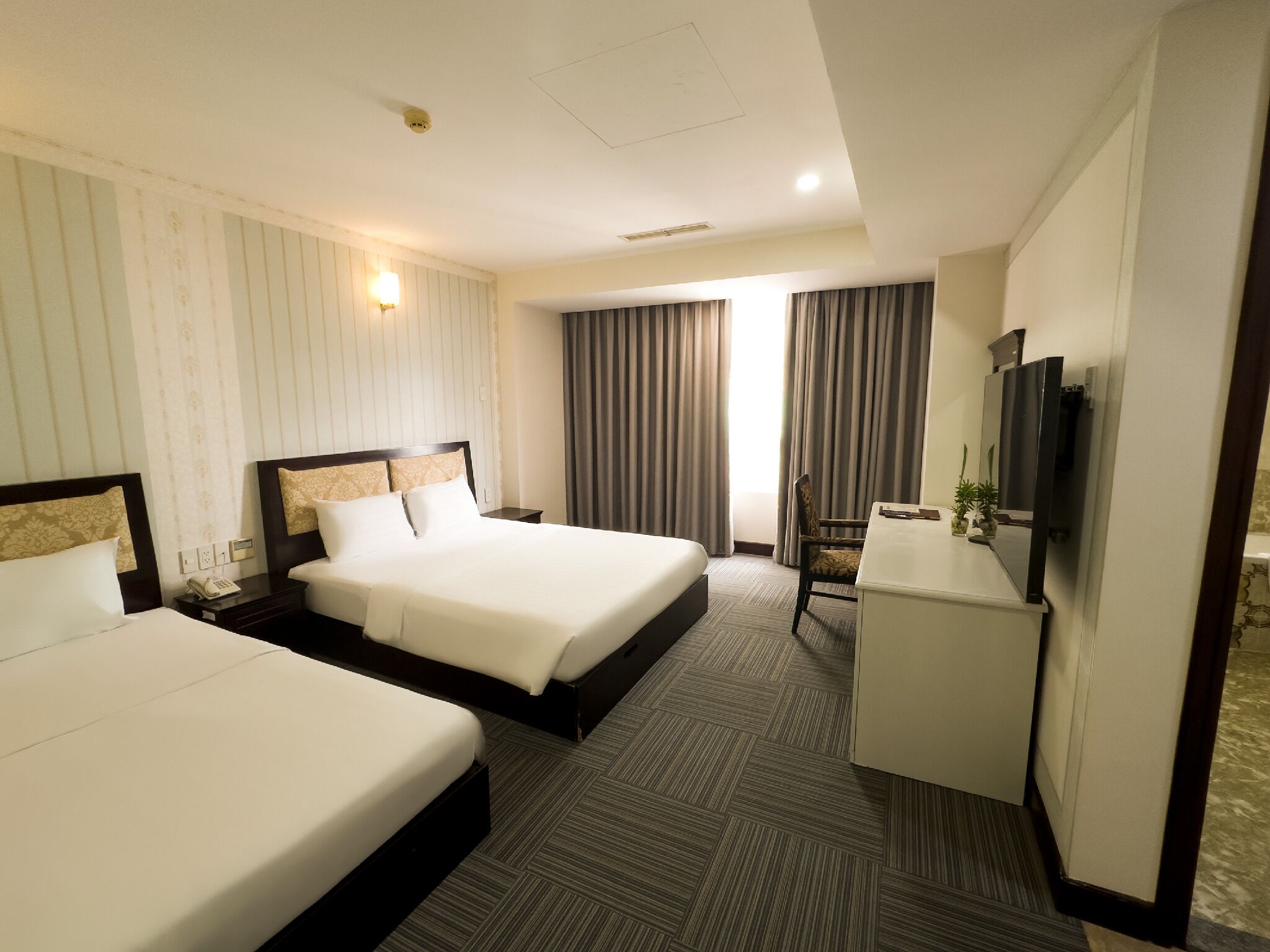 A hotel room with two beds, a desk, a chair, a television, and a window with curtains.