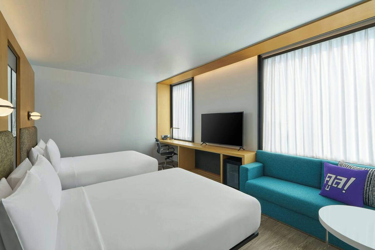 A hotel room with two beds, a TV, a sofa, and a small table.