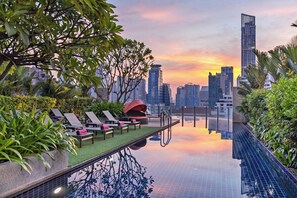 An infinity pool with lounge chairs and a cityscape view at sunset.