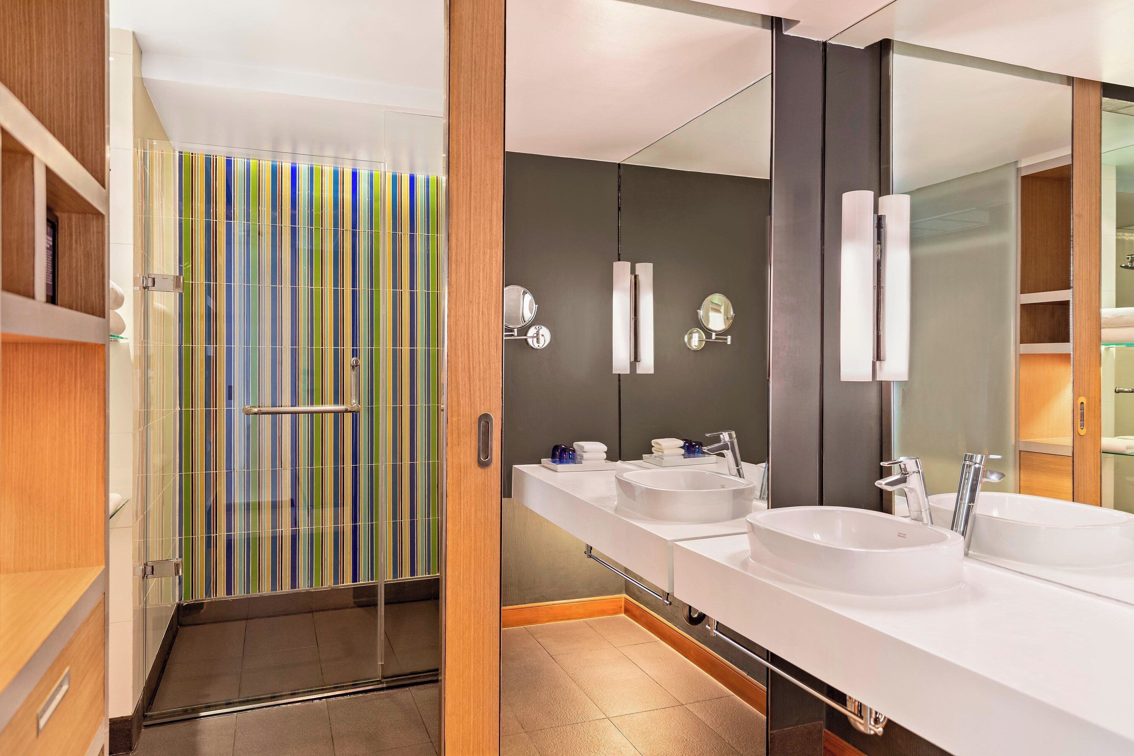 Een moderne badkamer met een grote spiegel, twee wastafels en een douche met een gestreepte glazen deur.
