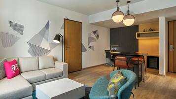 Una sala moderna con un sofá, una mesa de centro y un comedor con sillas y una mesa. Hay una zona de cocina con estufa y armarios.