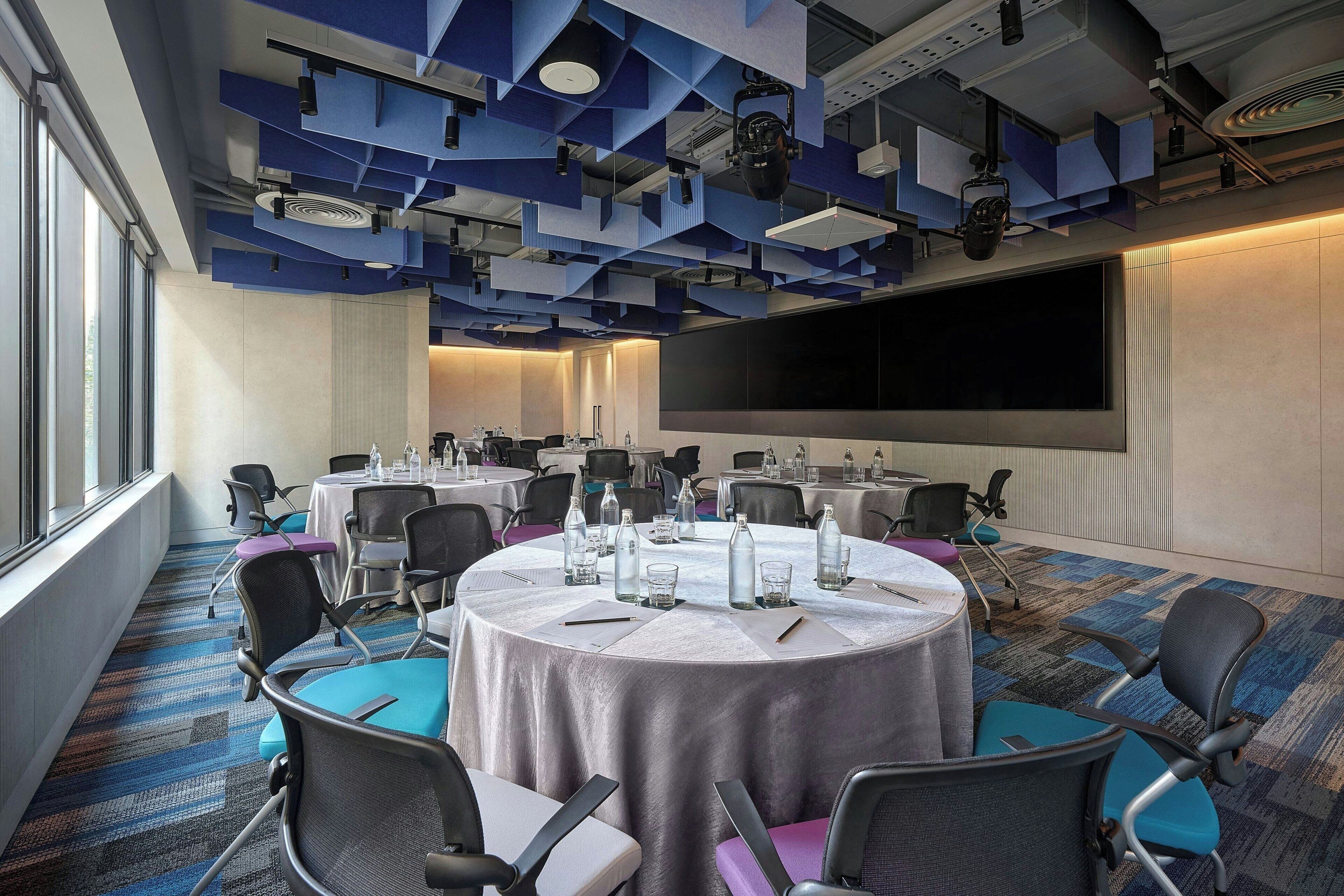 Un salón de conferencias con mesas redondas, sillas y una pantalla grande.