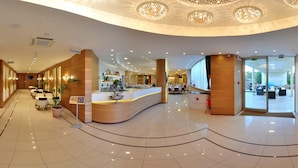 Un vestíbulo de hotel con una recepción, zona de estar y vistas al exterior.