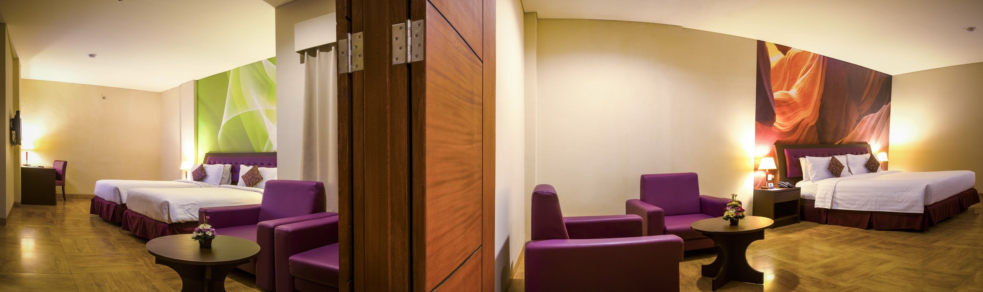 A hotel room with two beds, purple chairs, a small table, and a large painting on the wall.