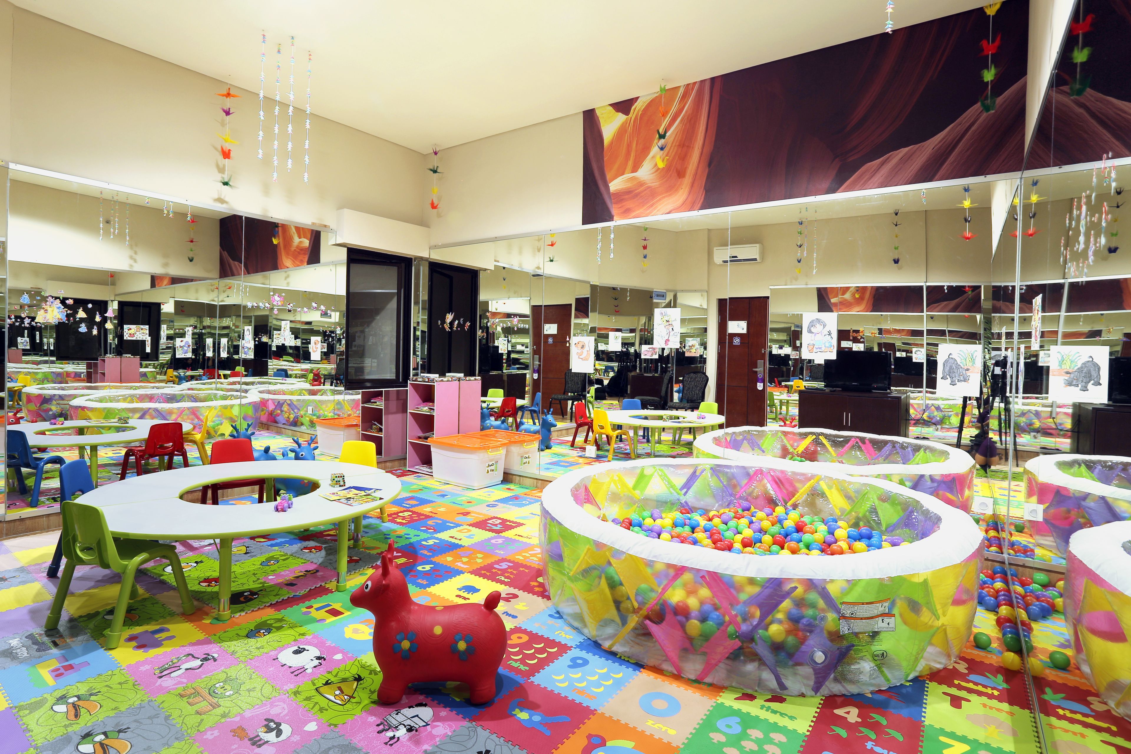 A children's play area with colorful play mats, tables, chairs, and a ball pit.