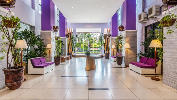 Un vestíbulo moderno con sofás blancos, plantas en macetas y una mesa de madera en el centro.