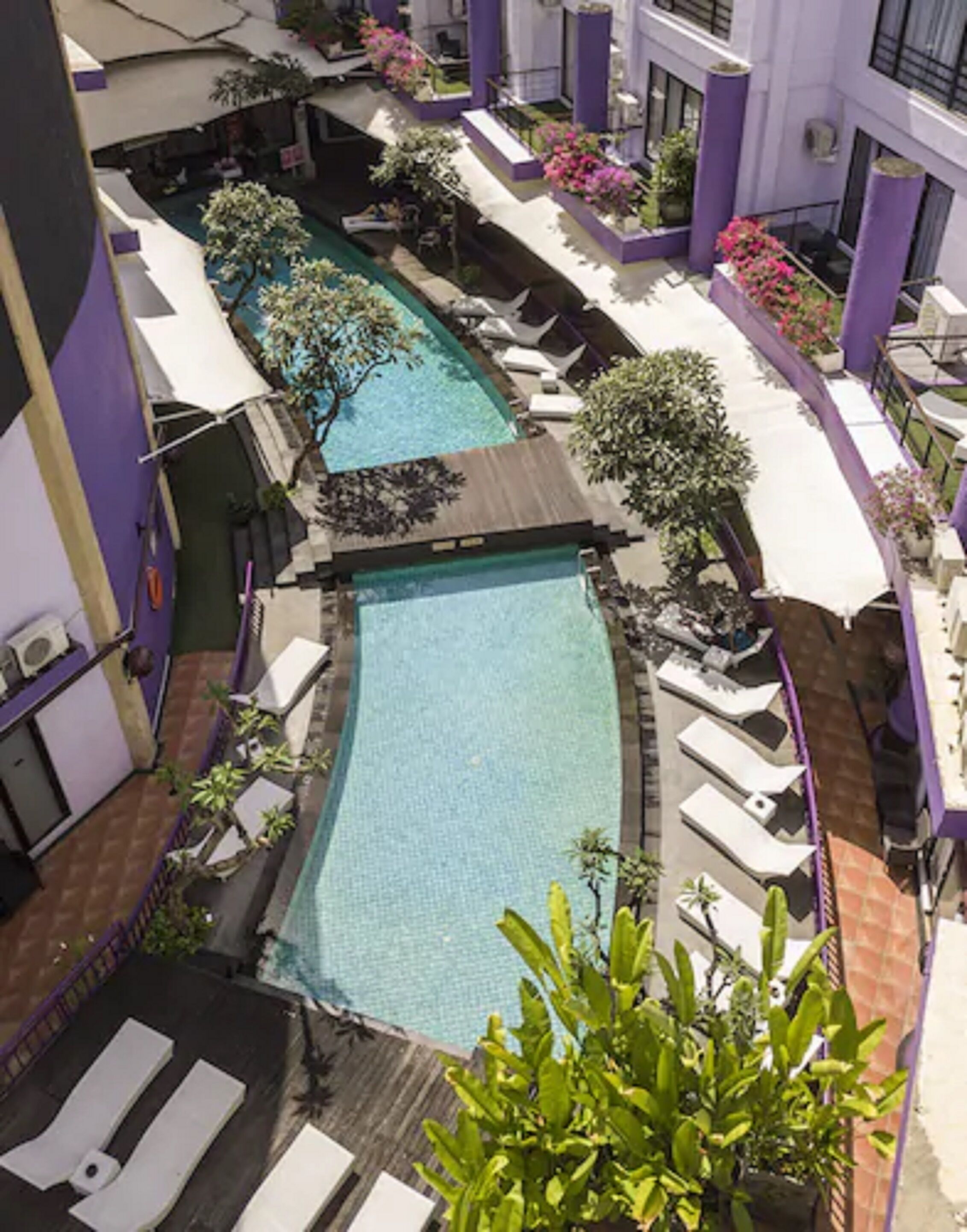A rooftop pool area with multiple swimming pools, lounge chairs, and potted plants.