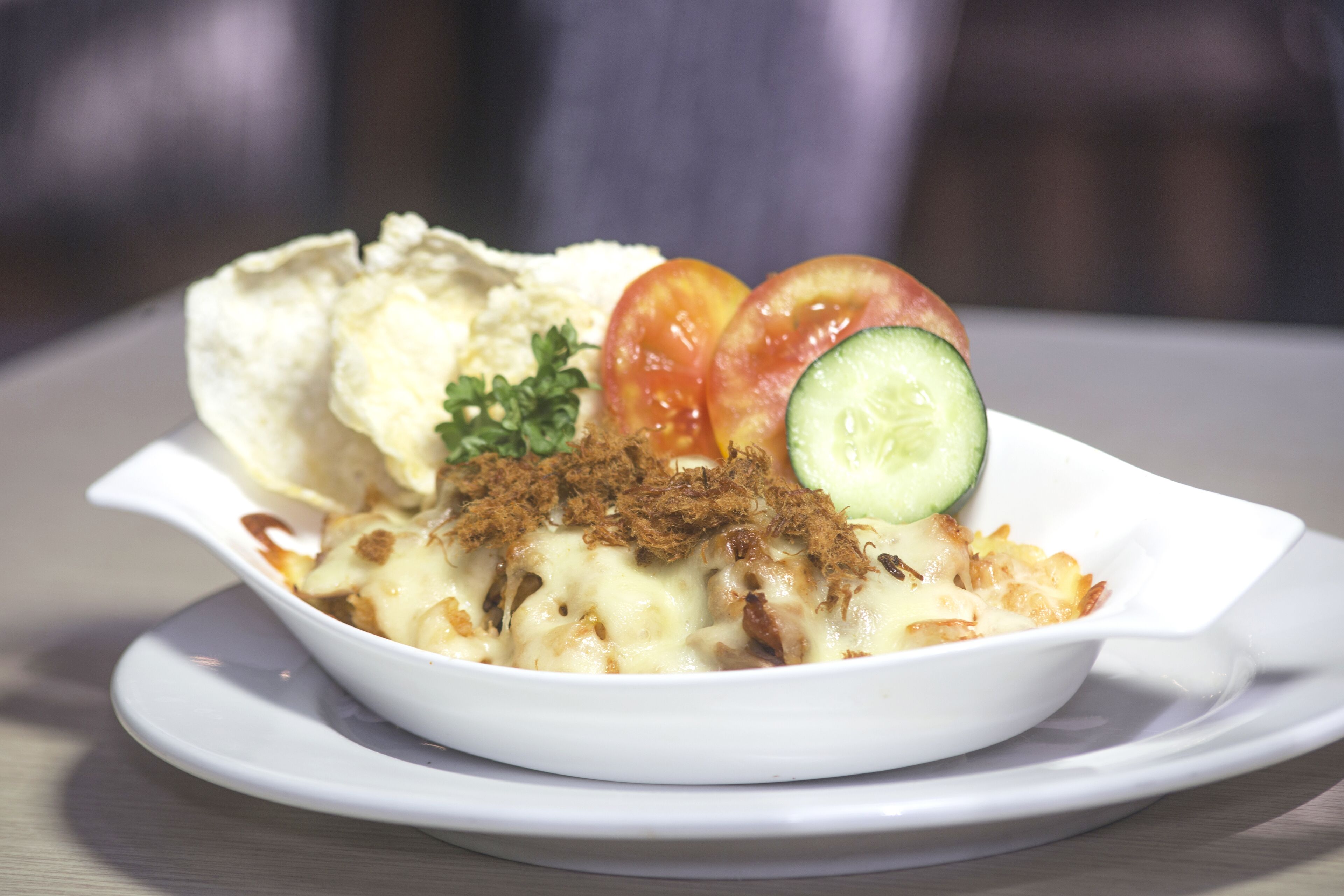 A white bowl of food with a side of chips and garnished with tomatoes, cucumber, and parsley.