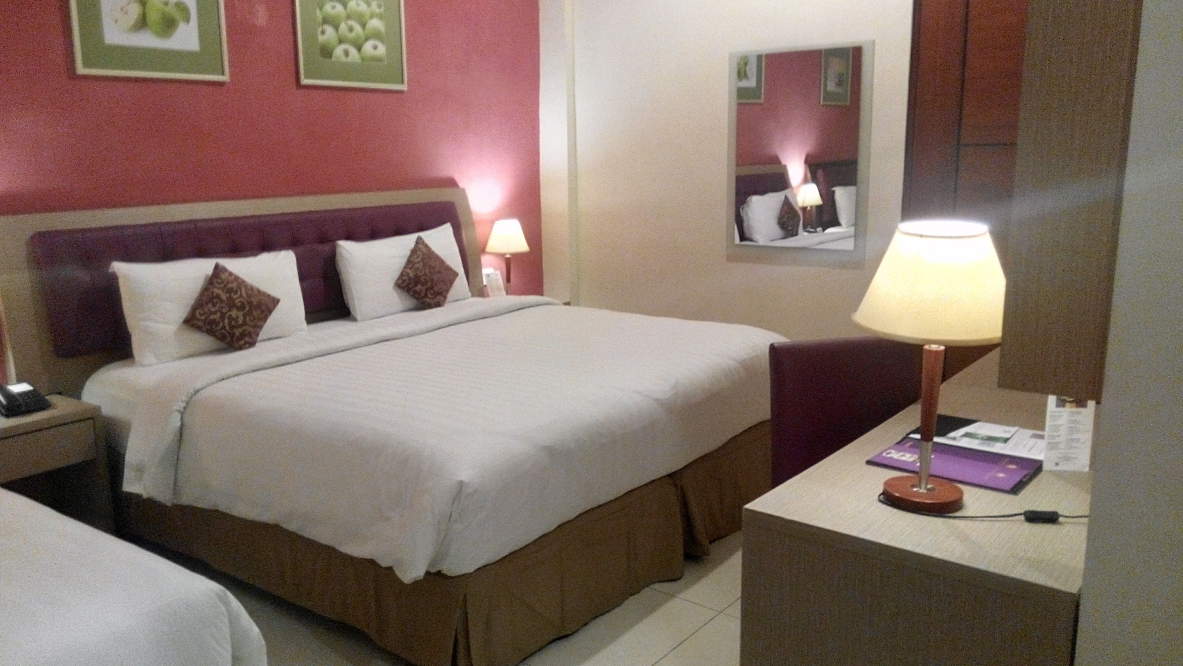 Ein Hotelzimmer mit Bett, Nachttisch, Lampe und Spiegel.