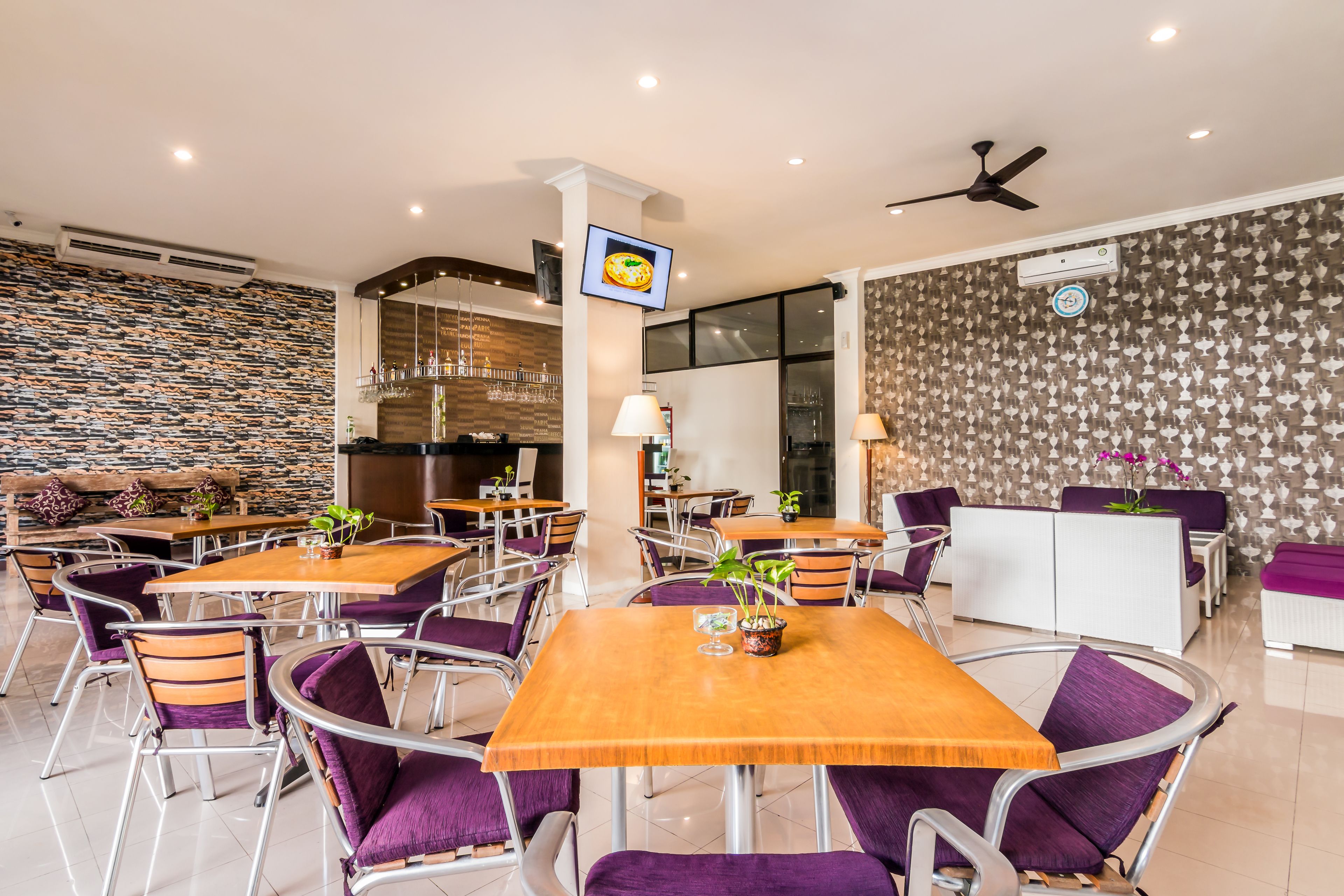 A modern dining area with multiple tables and chairs, a kitchen in the background, and a patterned wall.