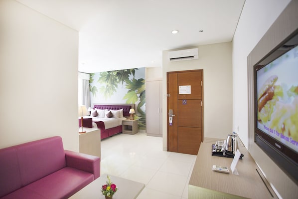 A hotel room with a bed, a sofa, a TV, and a door. - Kuta Central Park Hotel (Kuta)