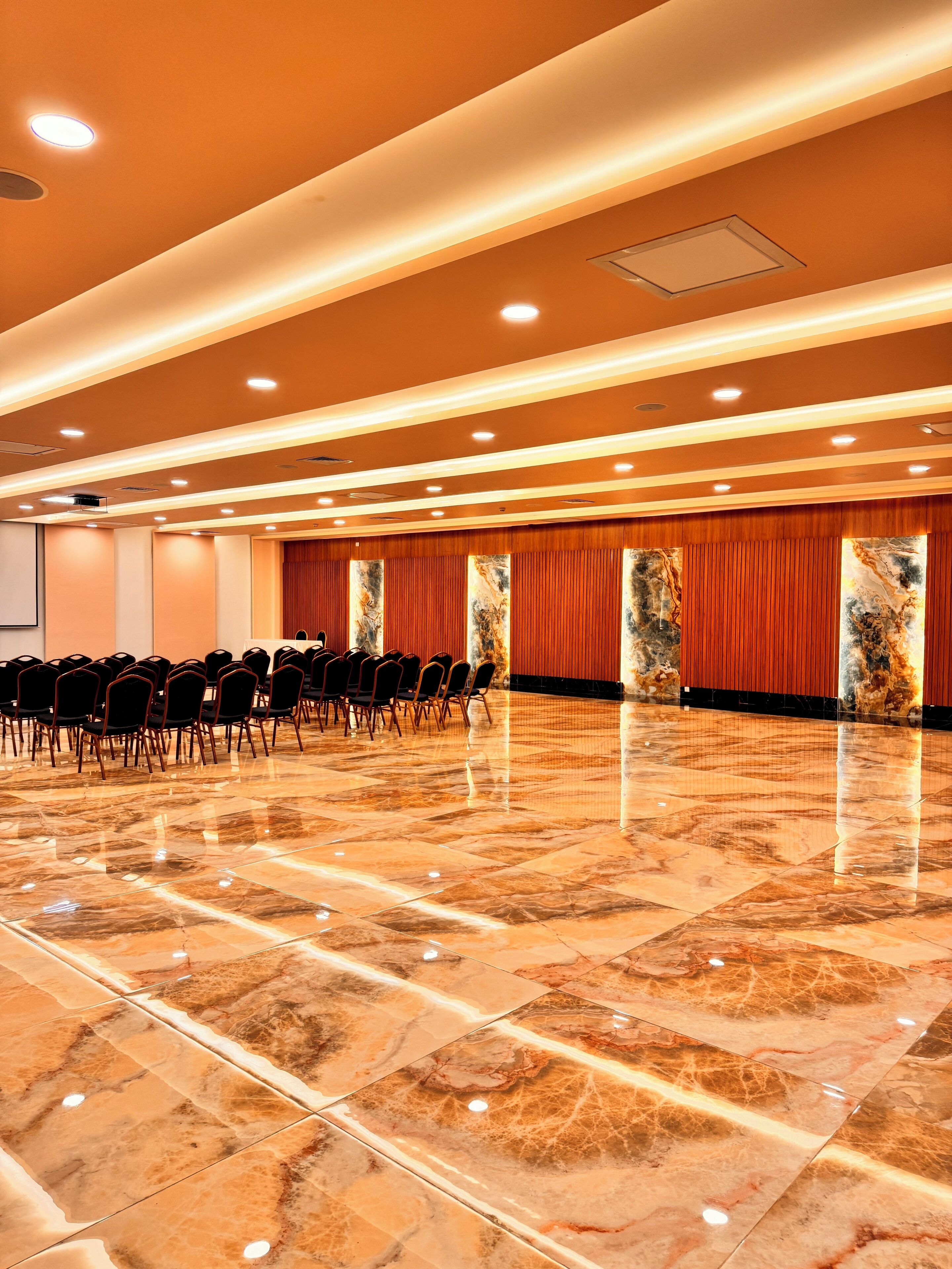 A spacious conference room with rows of chairs, a polished marble floor, and a high ceiling with recessed lighting.