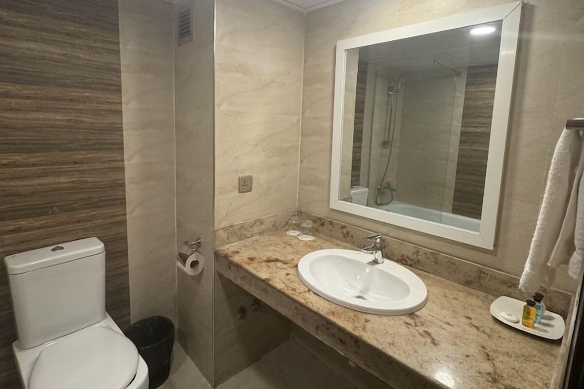 A bathroom with a toilet, sink, mirror, and shower.