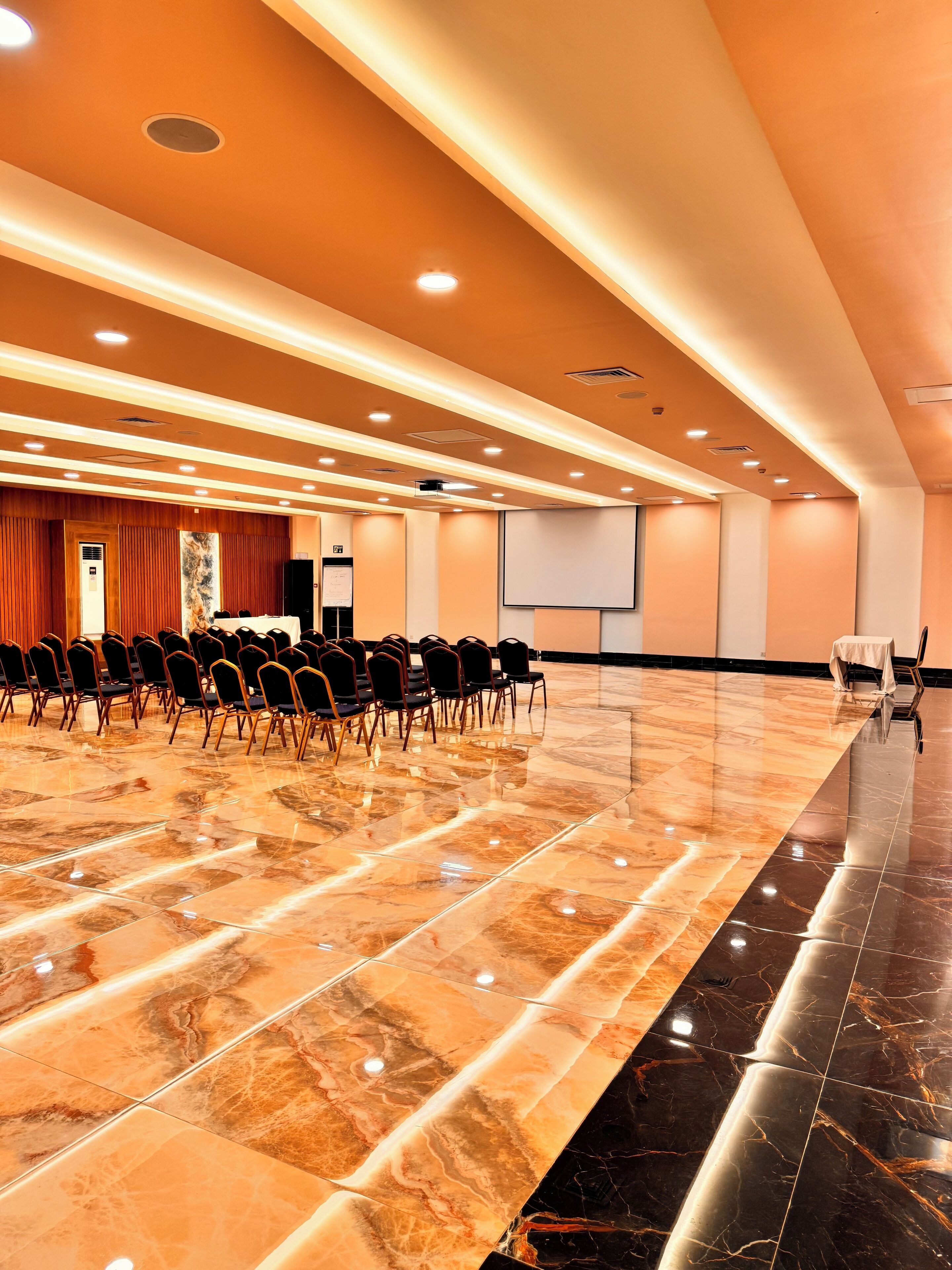 A conference room with a polished marble floor, rows of chairs, a podium, and a projector screen.