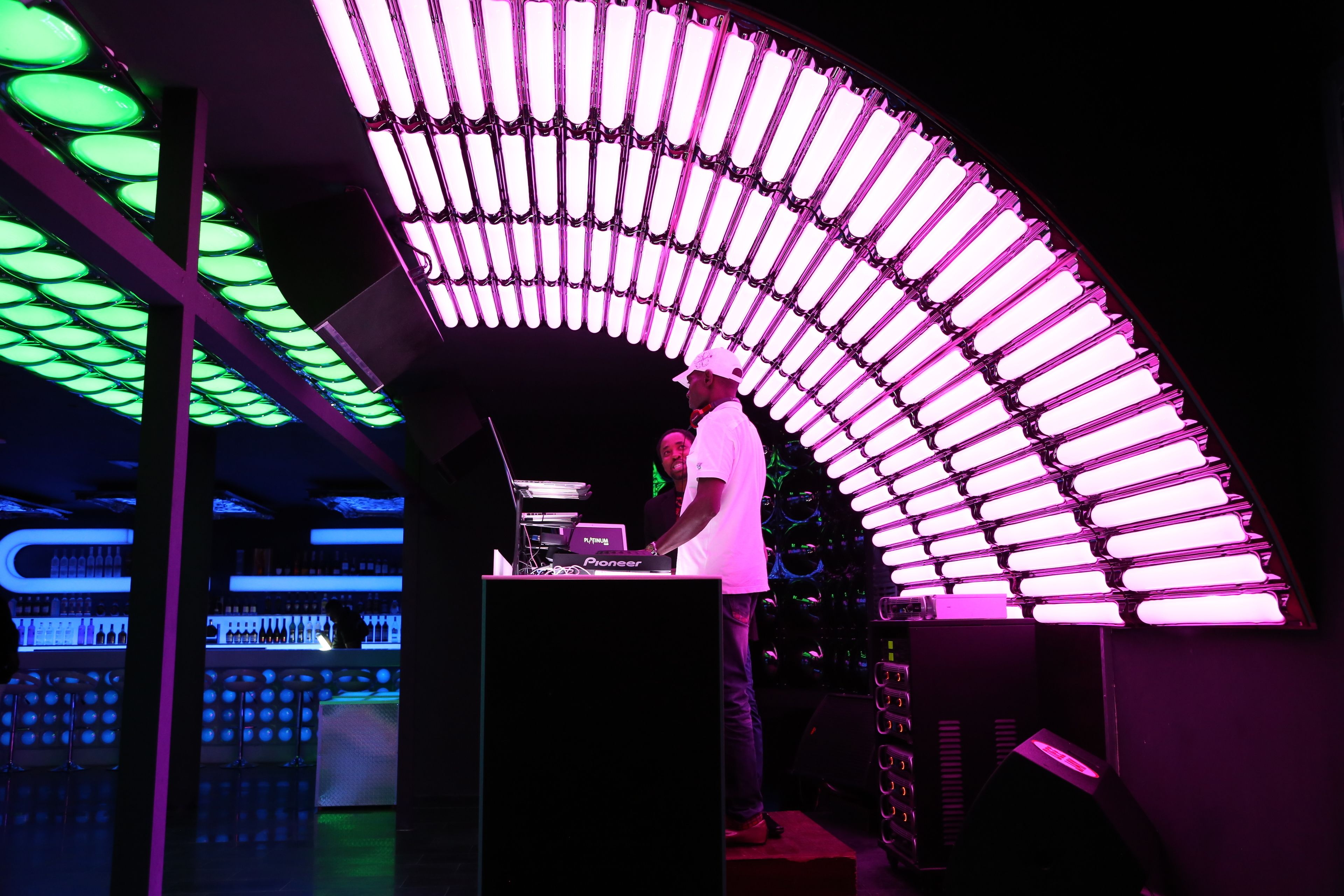 Une cabine de DJ dotée d’un luminaire au plafond à la forme incurvée et d’un bar avec des bouteilles.