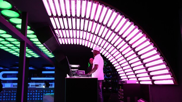 A DJ booth with a curved ceiling light fixture and a bar area with bottles. - Presidential Hotel (Port Harcourt)