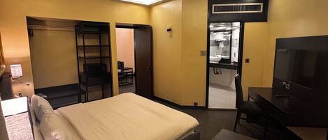 A hotel room with a bed, desk, chair, and a television. There is a bathroom visible through an open door.