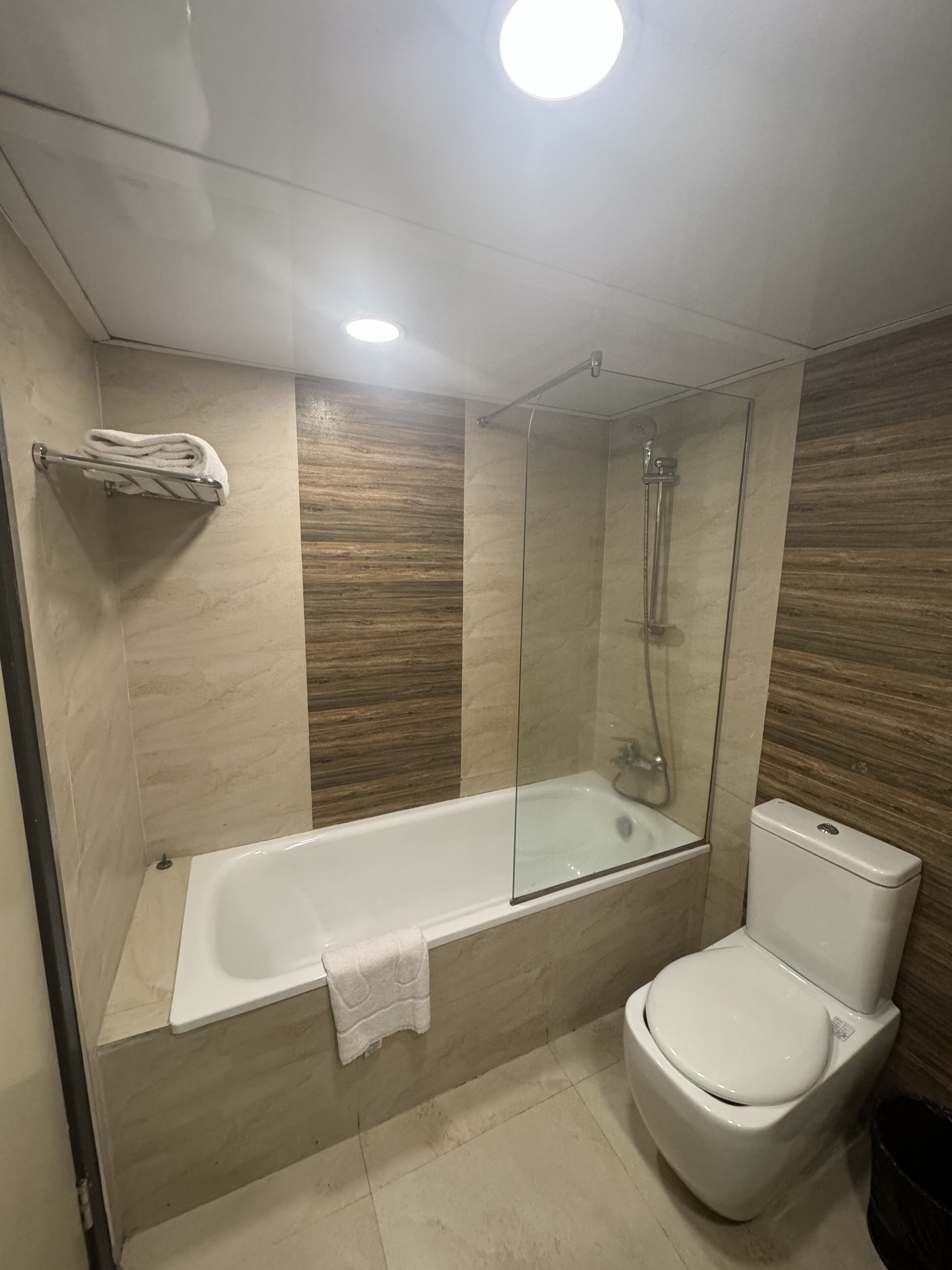 A modern bathroom with a glass-enclosed shower, a white bathtub, and a toilet.