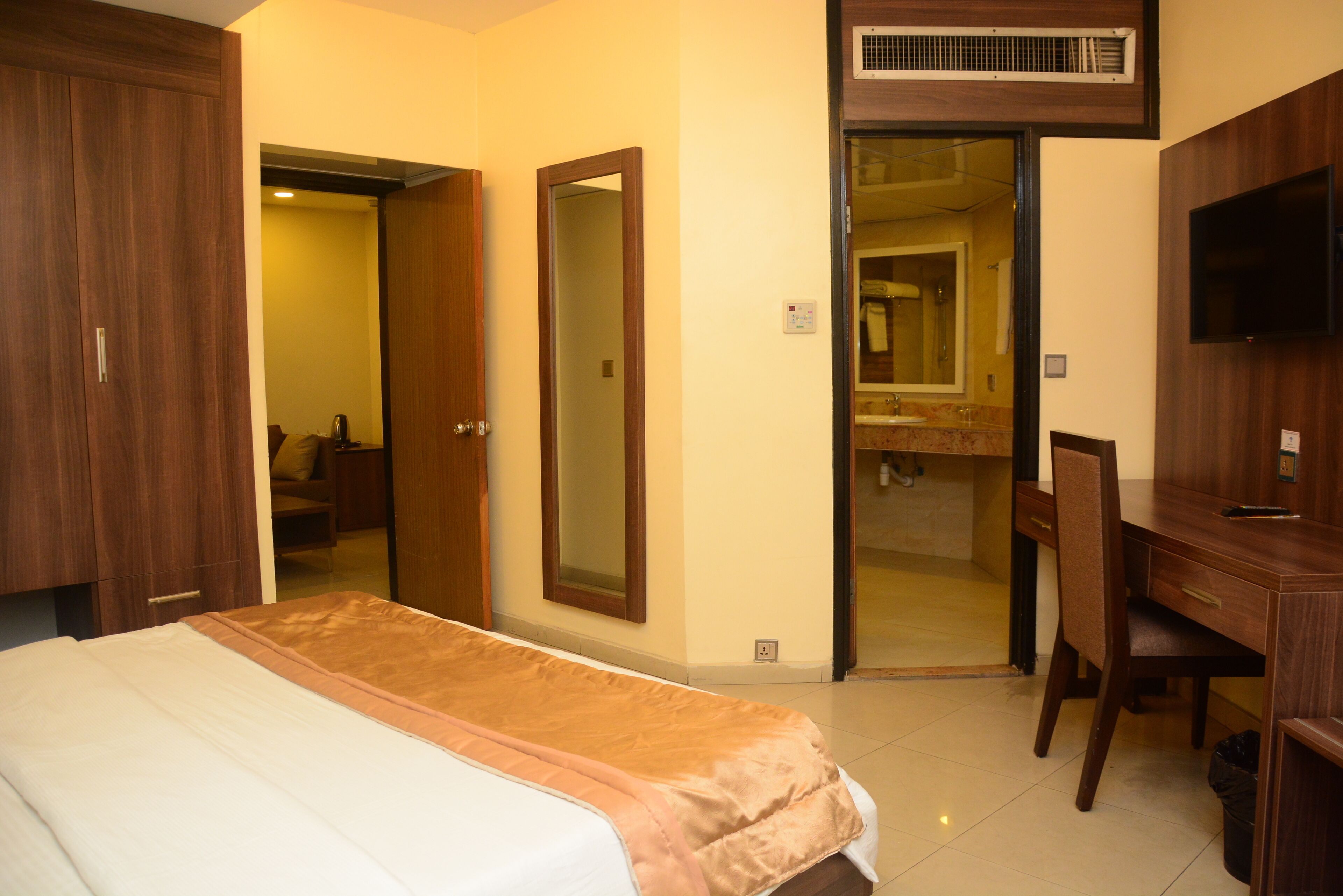 A hotel room with a bed, a desk, a chair, a mirror, and a bathroom visible through an open door.