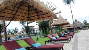 A row of sun loungers with thatched umbrellas, a paved walkway, and palm trees in the background. - Presidential Hotel (Port Harcourt)