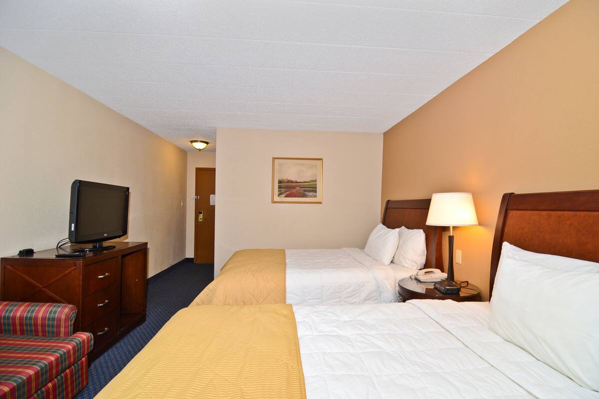 A hotel room with two beds, a television, a desk, and a chair.