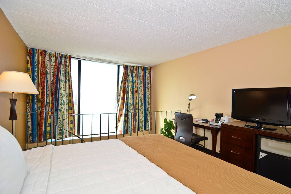 A hotel room with a bed, desk, TV, and curtains.