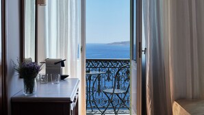 A balcony with a view of the sea, a vase with flowers, and a small table with a lamp and glasses.
