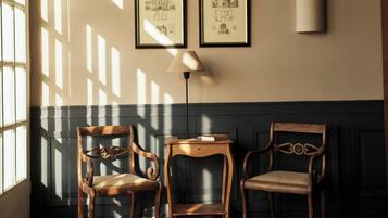 Una habitación con suelo de madera, dos sillas, una mesa, una lámpara y dos cuadros en la pared.