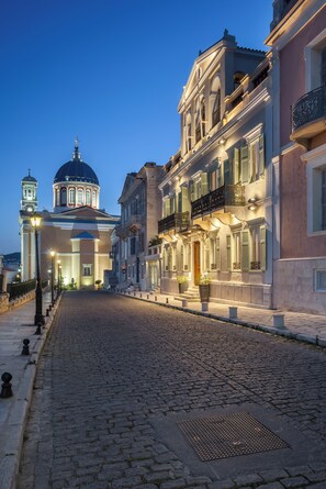 A cobblestone street lined with historic buildings, including a church with a dome and bell tower, and a building with balconies and ornate railings.