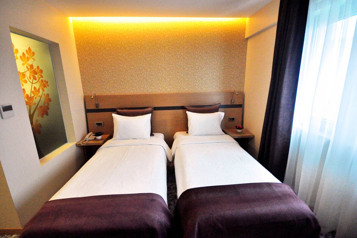 Een hotelkamer met twee bedden, een nachtkastje met een telefoon en een schilderij aan de muur.