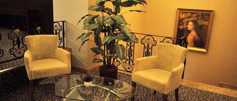 A lobby with two armchairs, a glass coffee table, a potted plant, and a framed artwork on the wall.