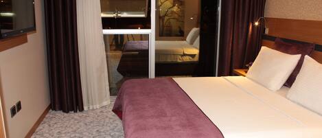 Habitación de hotel con una cama grande, un televisor de pantalla plana y una puerta de cristal corredera que da a un balcón.