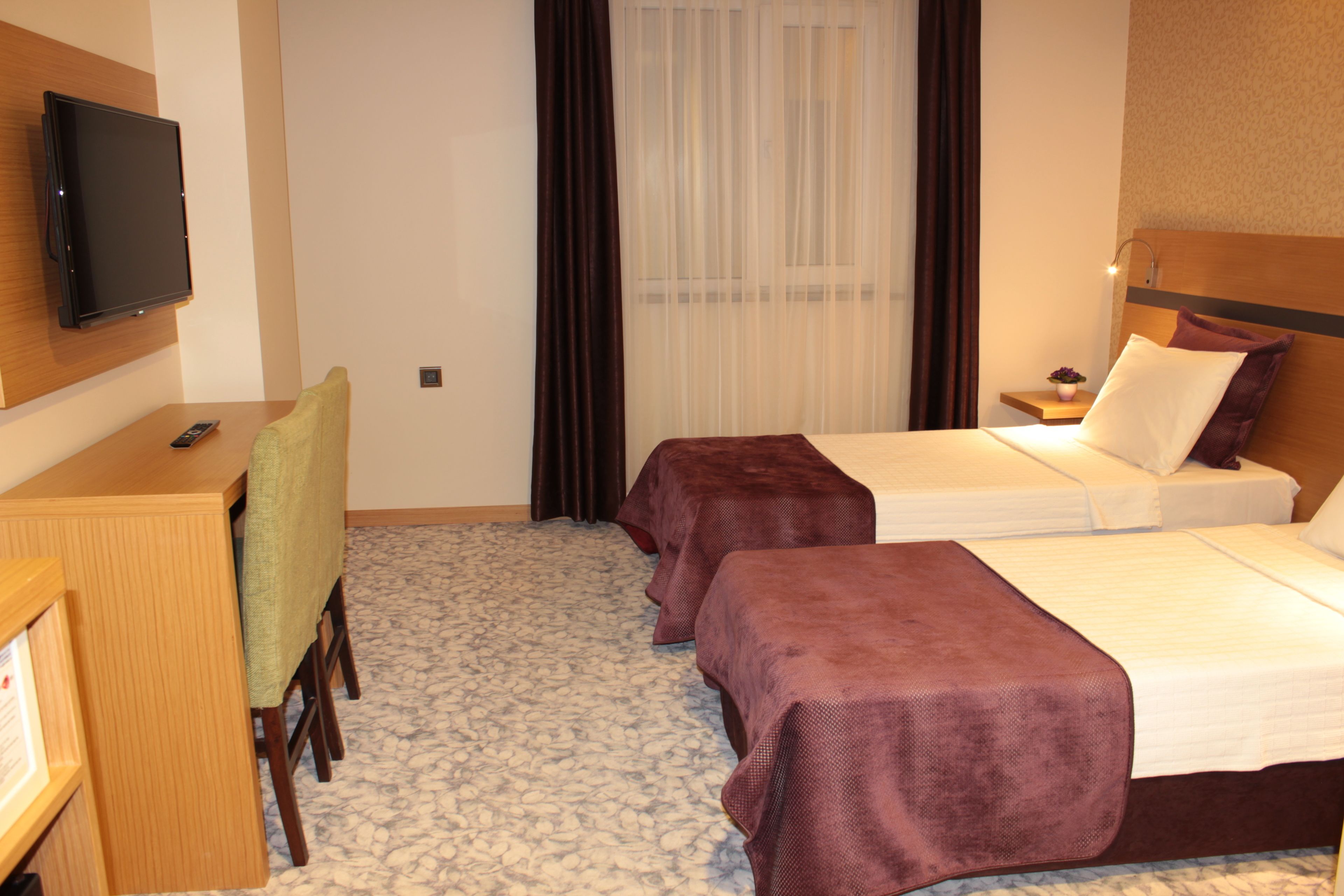 Ein Hotelzimmer mit zwei Betten, einem Schreibtisch mit Stuhl, einem Fernseher und einem Fenster mit Vorhängen.