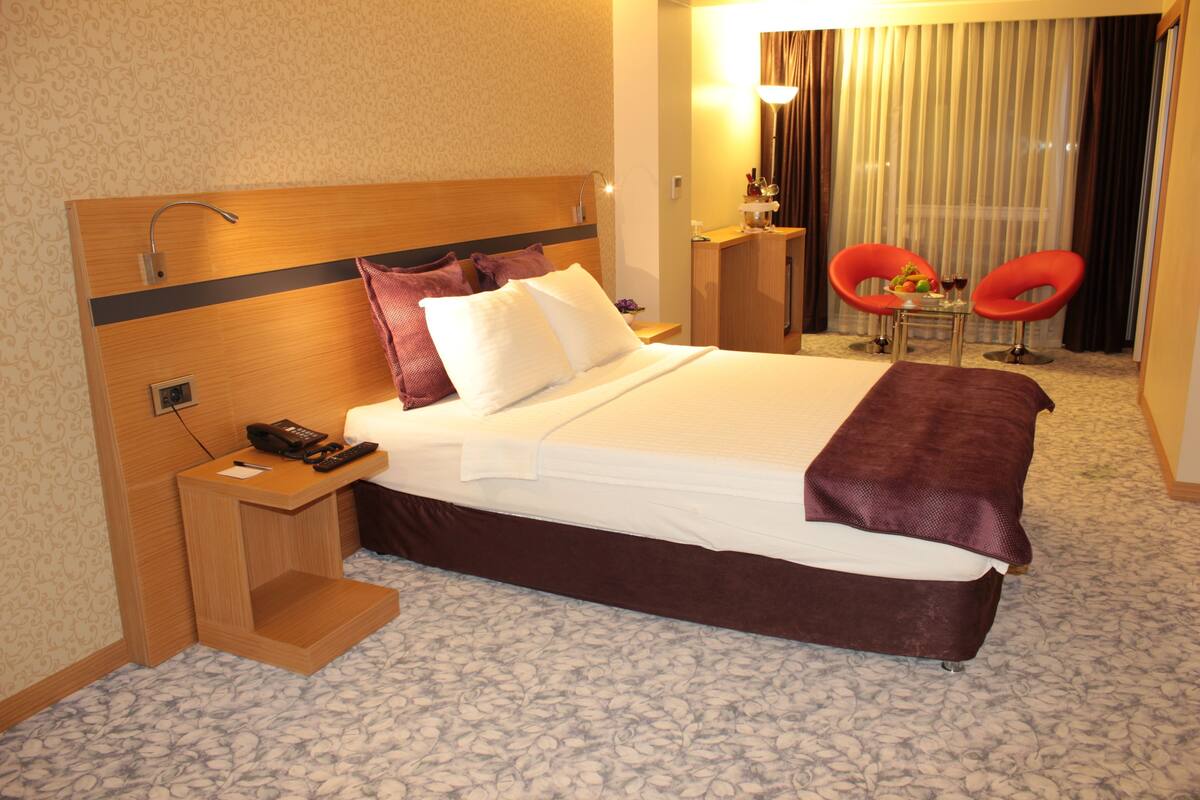 Een hotelkamer met een bed, nachtkastje, lamp en twee rode stoelen.
