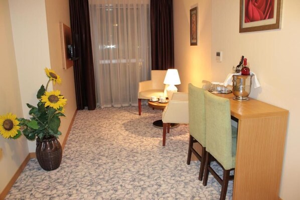 Quarto de hotel com área de refeições, um vaso de girassóis, uma luminária e uma mesa com garrafa e copos.