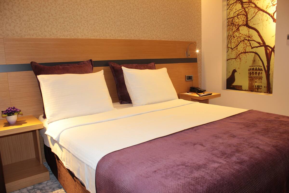 Een hotelkamer met een bed, nachtkastje, lamp en een aan de muur hangend schilderij.