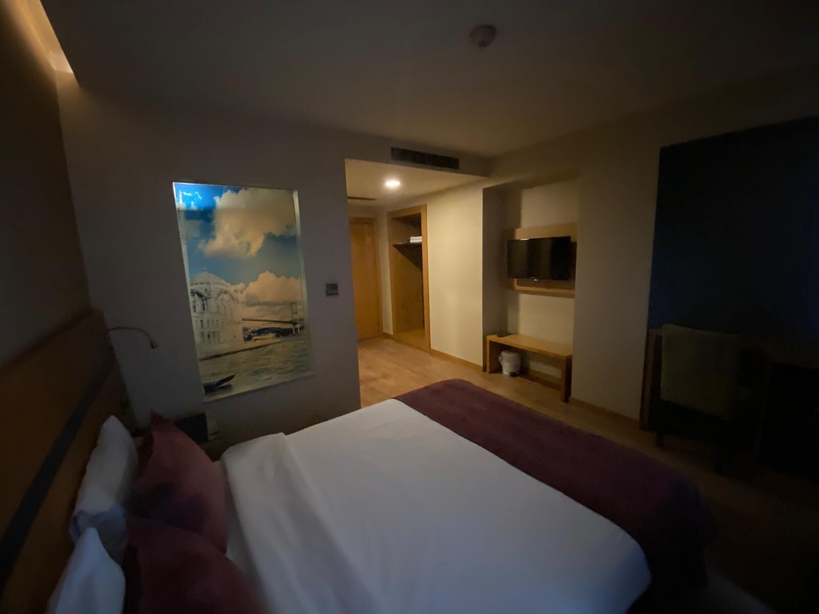 Een hotelkamer met een groot bed, een televisie en een schilderij van een stadsgezicht.